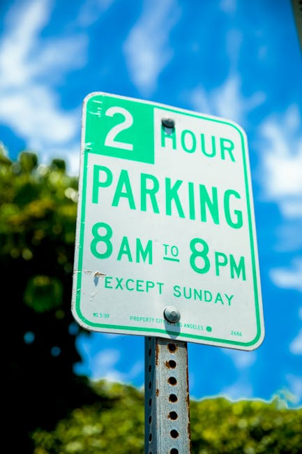 A close-up view of a green and white parking restriction sign mounted on a metal post in an outdoor setting. The sign indicates a two-hour parking limit from 8 am to 8 pm, with exemption on Sundays. I